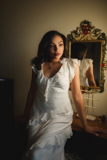 Kierra Sari in a white dress beside a vintage mirror